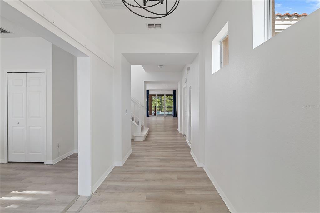A bright hallway features light wood-look flooring, white walls, and a staircase leading upstairs — 410 LAS FUENTES DRIVE, KISSIMMEE, FL