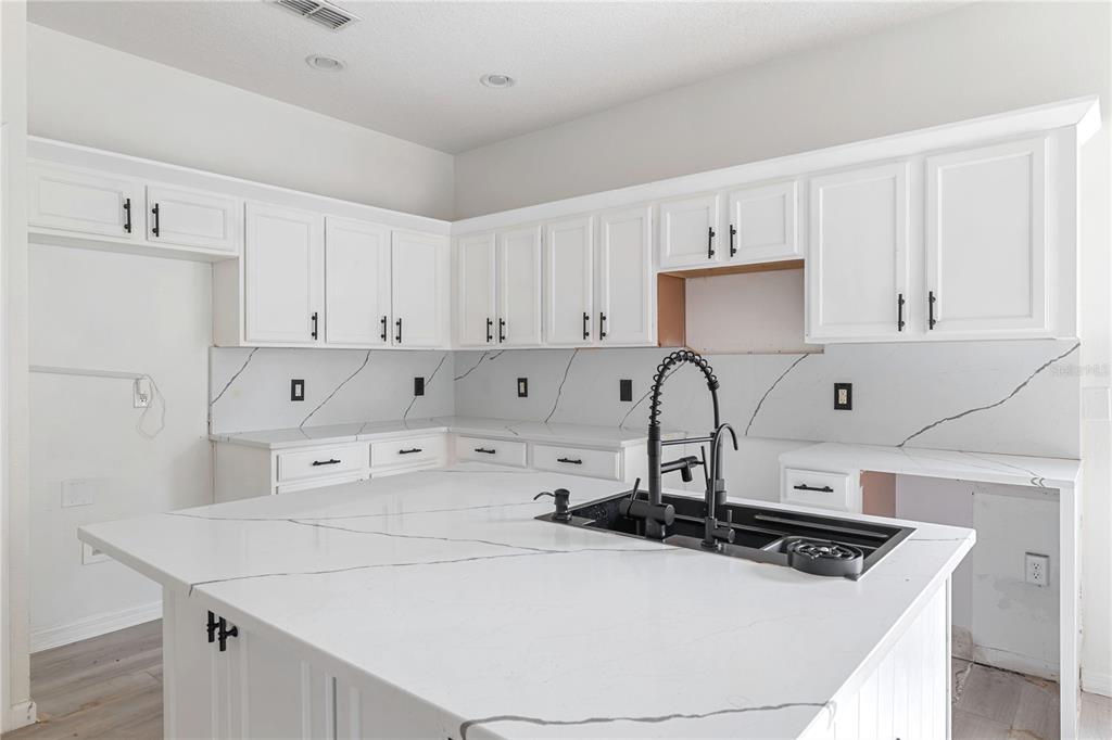 A kitchen features white cabinets, a large island with a black sink, and marble-patterned countertops — 410 LAS FUENTES DRIVE, KISSIMMEE, FL