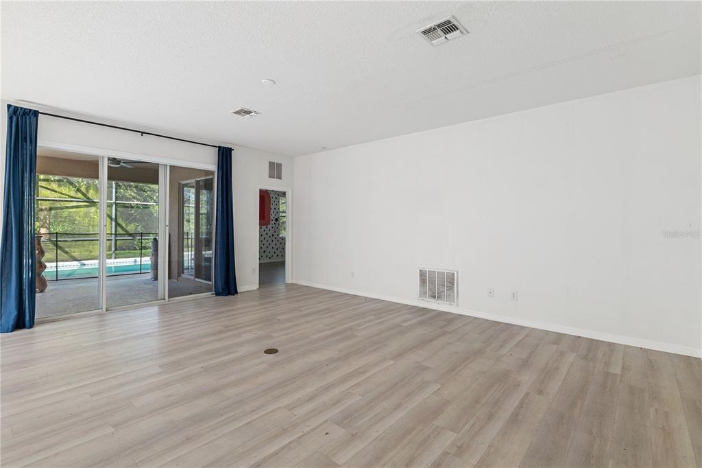 A living room with light wood-look flooring, white walls, and sliding glass doors to a pool — 410 LAS FUENTES DRIVE, KISSIMMEE, FL