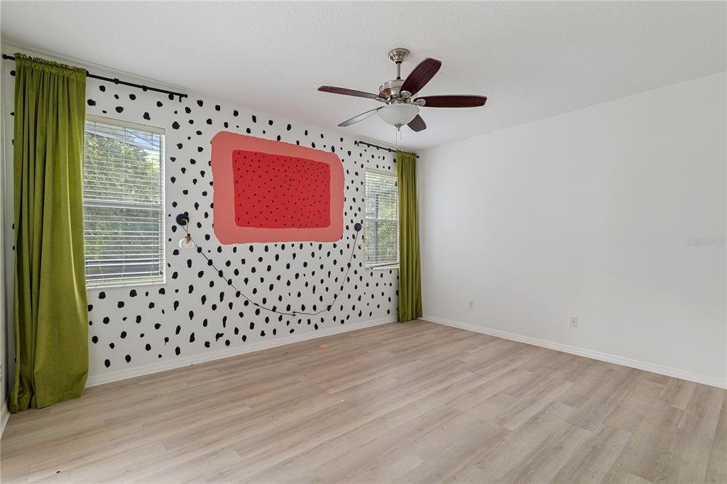 A bedroom features light wood-look flooring, green curtains, and a wall with black-and-white polka dots — 410 LAS FUENTES DRIVE, KISSIMMEE, FL