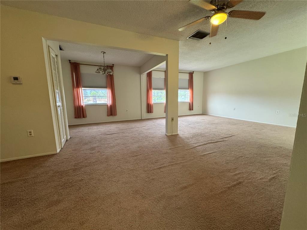 An open-concept living and dining area features beige carpeting, neutral walls, and a ceiling fan — 1126 KING ARTHUR COURT UNIT 413, DUNEDIN, FL