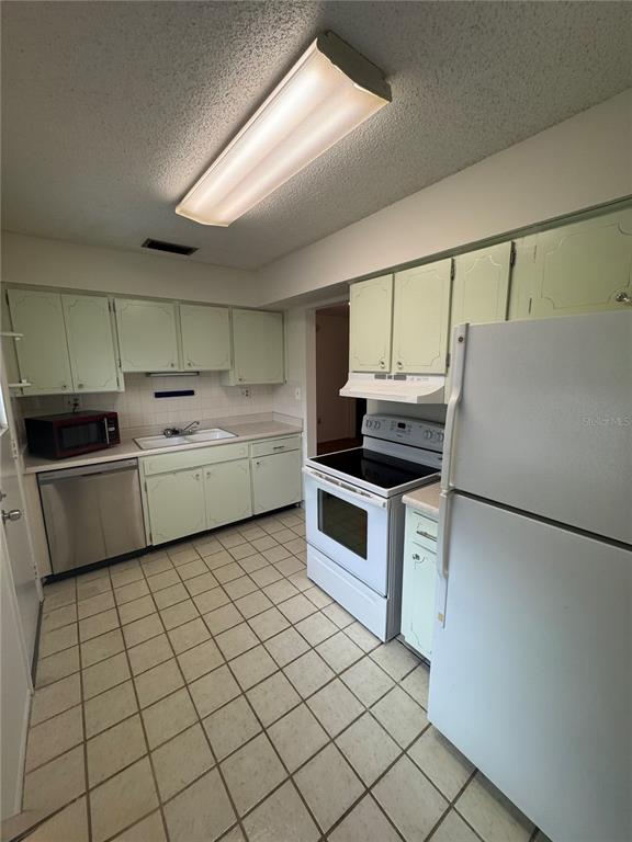 A kitchen features light green cabinets, white appliances, a tiled floor, and a fluorescent light — 1126 KING ARTHUR COURT UNIT 413, DUNEDIN, FL