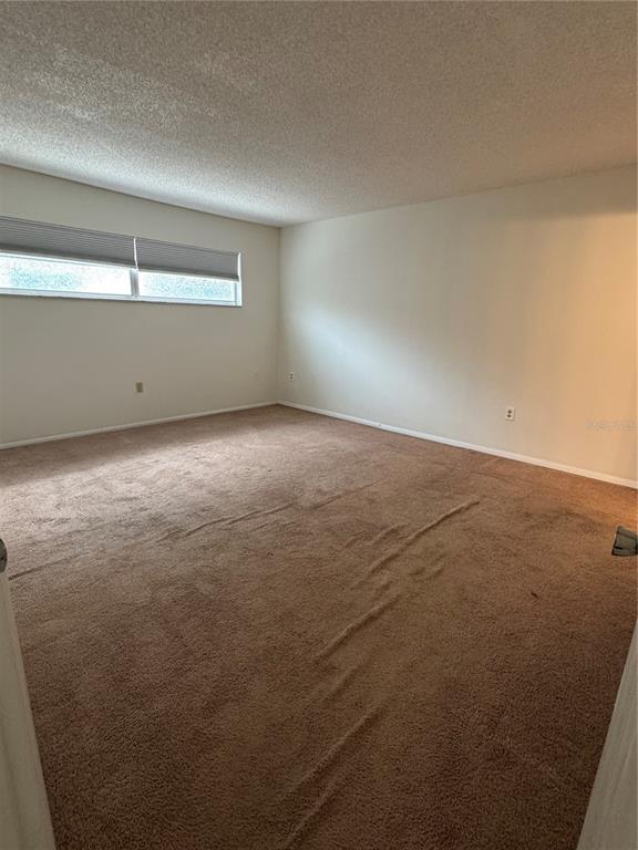 An empty bedroom features beige carpet, off-white walls, and a window with pleated shades — 1126 KING ARTHUR COURT UNIT 413, DUNEDIN, FL