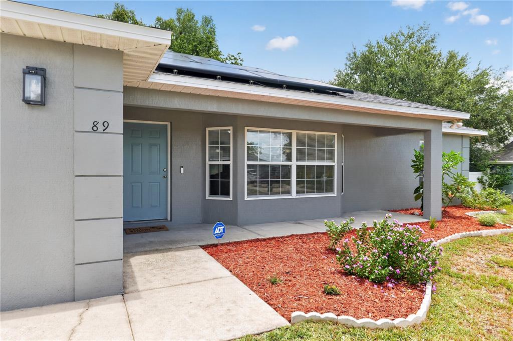 The exterior of a gray house features a light blue front door and solar panels — 89 PECAN COURSE CIRCLE, OCALA, FL