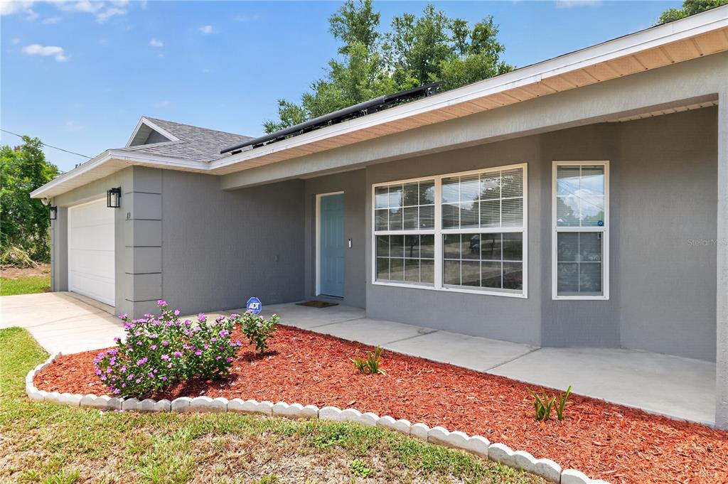 A gray house exterior features a white garage door, a blue front door, and landscaping — 89 PECAN COURSE CIRCLE, OCALA, FL