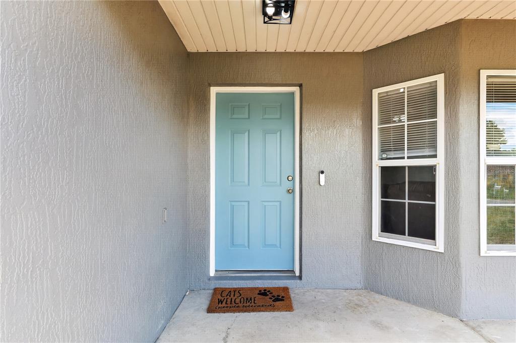 A light blue front door with a welcome mat sits under a covered porch — 89 PECAN COURSE CIRCLE, OCALA, FL