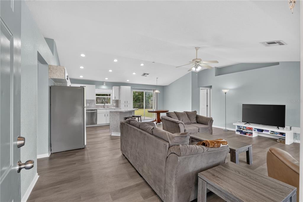 An open-concept living room and kitchen featuring light blue walls and wood-look flooring — 89 PECAN COURSE CIRCLE, OCALA, FL