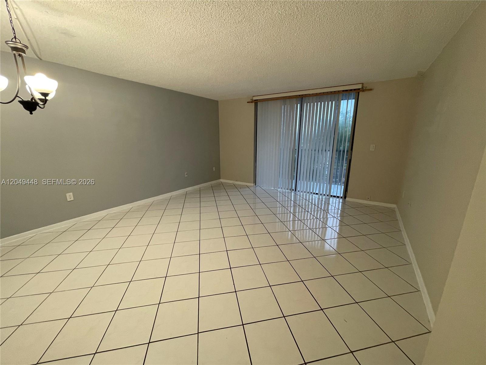 An empty room features white tiled floors, a grey accent wall, and sliding glass doors — 8400 SW 133rd Ave Rd # 424, Miami FL 33183, MIAMI, FL