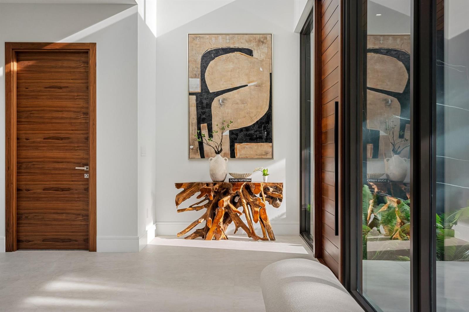 A modern entryway features a wooden root console table, abstract wall art, and a wood door — 2000 Harbourview Drive, Fort Lauderdale FL 33316, FORT LAUDERDALE, FL