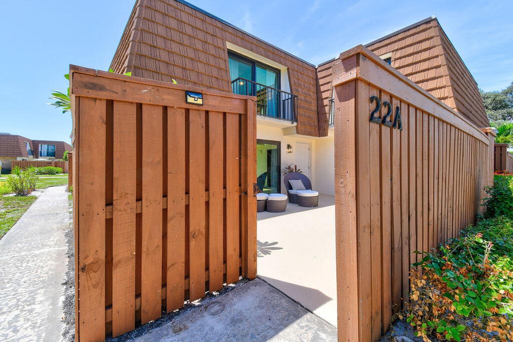 A wooden fence gate opens to a private patio entrance of a two-story townhouse — 3900 SE County Line Road # 22a, Jupiter FL 33469, JUPITER, FL