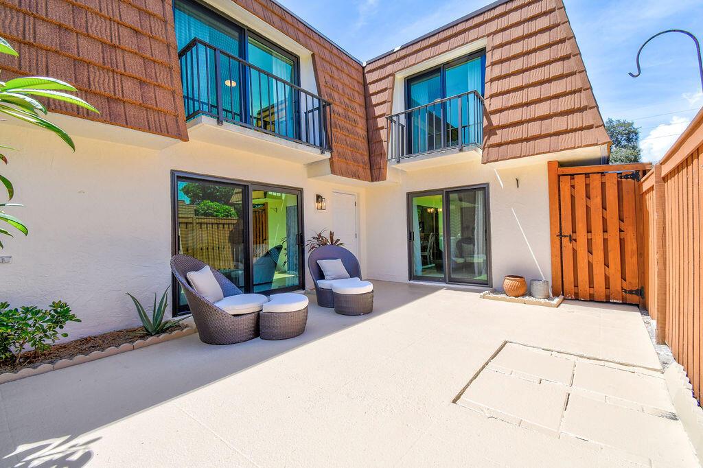 A patio with two wicker chairs and ottomans sits outside a two-story townhouse exterior — 3900 SE County Line Road # 22a, Jupiter FL 33469, JUPITER, FL