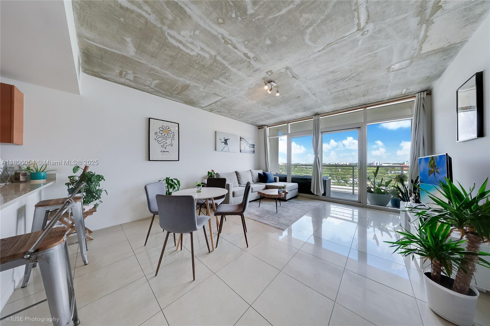 A modern living and dining area features a concrete ceiling, tile floors, and balcony access — 3250 NE 1st Ave # 1007, Miami FL 33137, MIAMI, FL