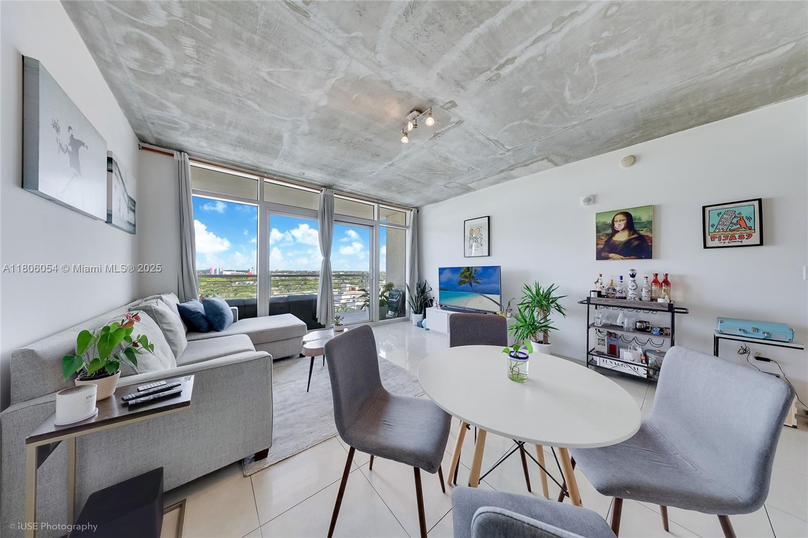A modern living and dining area features a concrete ceiling, white tile floors, and balcony access — 3250 NE 1st Ave # 1007, Miami FL 33137, MIAMI, FL