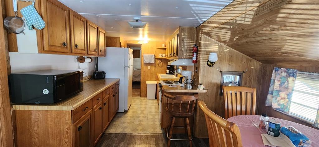 A kitchen with wood cabinets, a microwave, a white refrigerator, and a small dining area — 138 FLAMINGO STREET, DAVENPORT, FL
