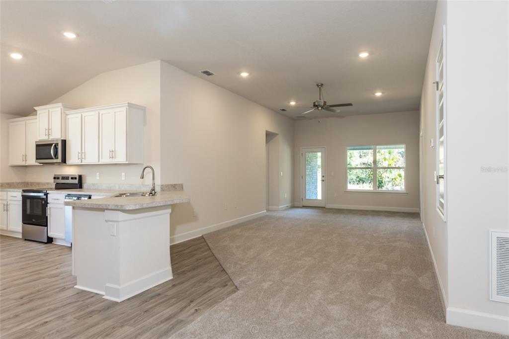 A kitchen with white cabinets and a peninsula opens into a carpeted living area — 54 PONY EXPRESS DRIVE, PALM COAST, FL