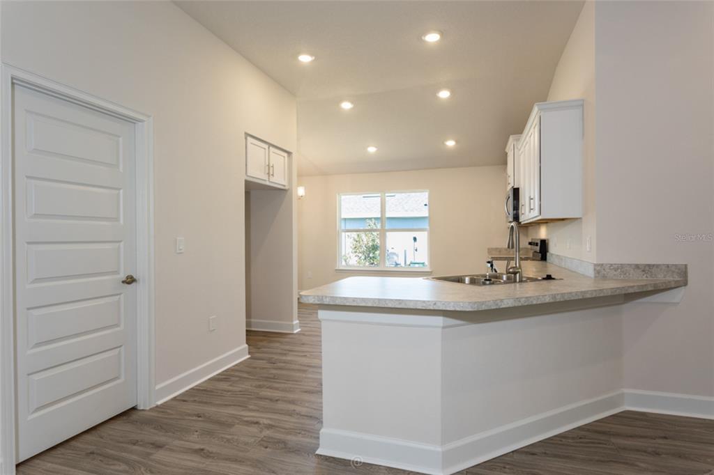 A kitchen with white cabinets, a breakfast bar, and wood-look flooring in an open space — 54 PONY EXPRESS DRIVE, PALM COAST, FL