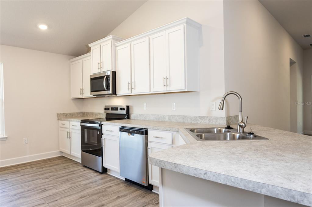 A kitchen with white cabinets, stainless steel appliances, and light gray laminate countertops — 54 PONY EXPRESS DRIVE, PALM COAST, FL