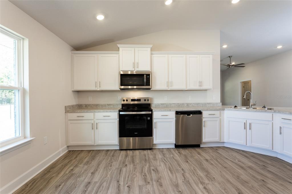 A kitchen with white cabinets, stainless steel appliances, and wood-look flooring — 54 PONY EXPRESS DRIVE, PALM COAST, FL