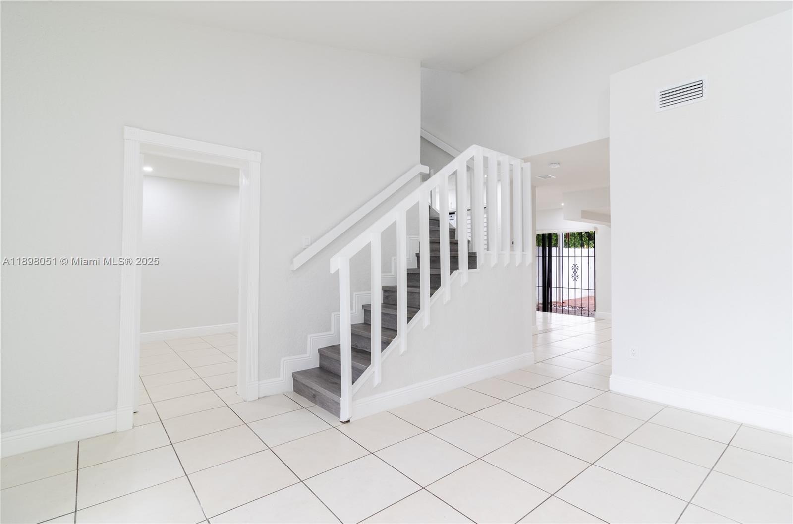 A staircase with dark wood treads and white railings sits in a white-tiled room — 217 NW 109th Ave # 217, Miami FL 33172, MIAMI, FL