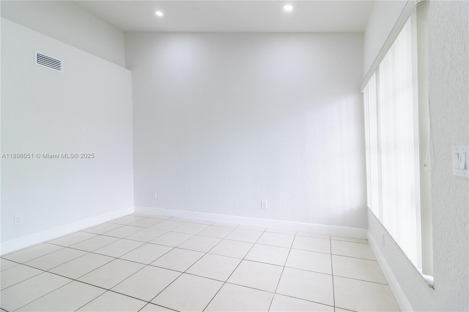 An empty room features white walls, light-colored tile flooring, recessed lighting, and a large window — 217 NW 109th Ave # 217, Miami FL 33172, MIAMI, FL