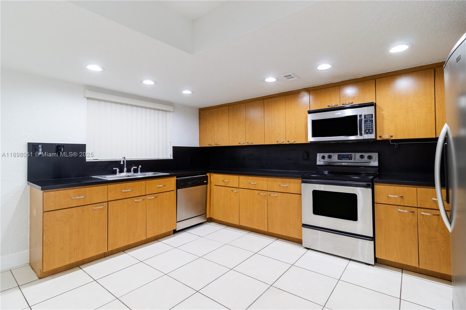 A kitchen features light wood cabinets, black countertops, stainless steel appliances, and white tile flooring — 217 NW 109th Ave # 217, Miami FL 33172, MIAMI, FL