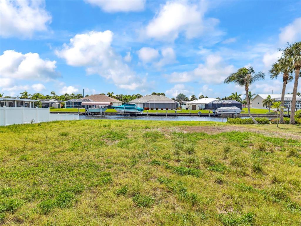 A vacant grassy lot overlooks a canal with boat docks and houses in the background — 4366 WYNKOOP CIRCLE, PORT CHARLOTTE, FL