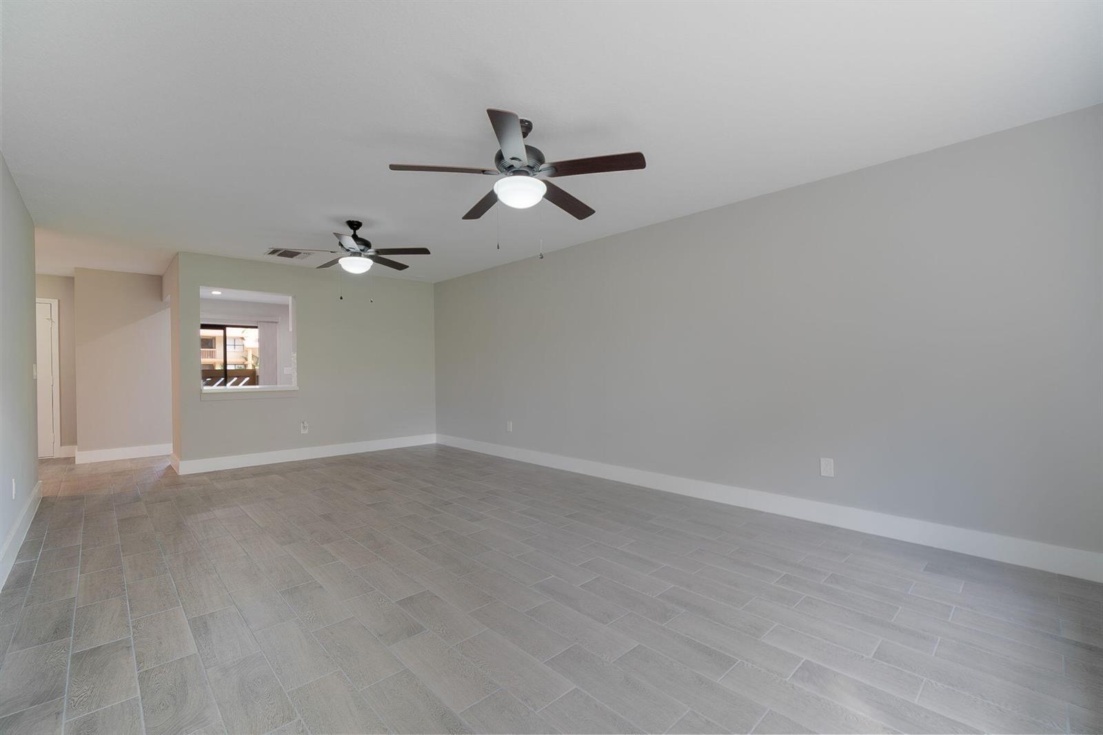 An empty room with gray wood-look tile flooring, two ceiling fans, and a pass-through window — WELLINGTON, FL