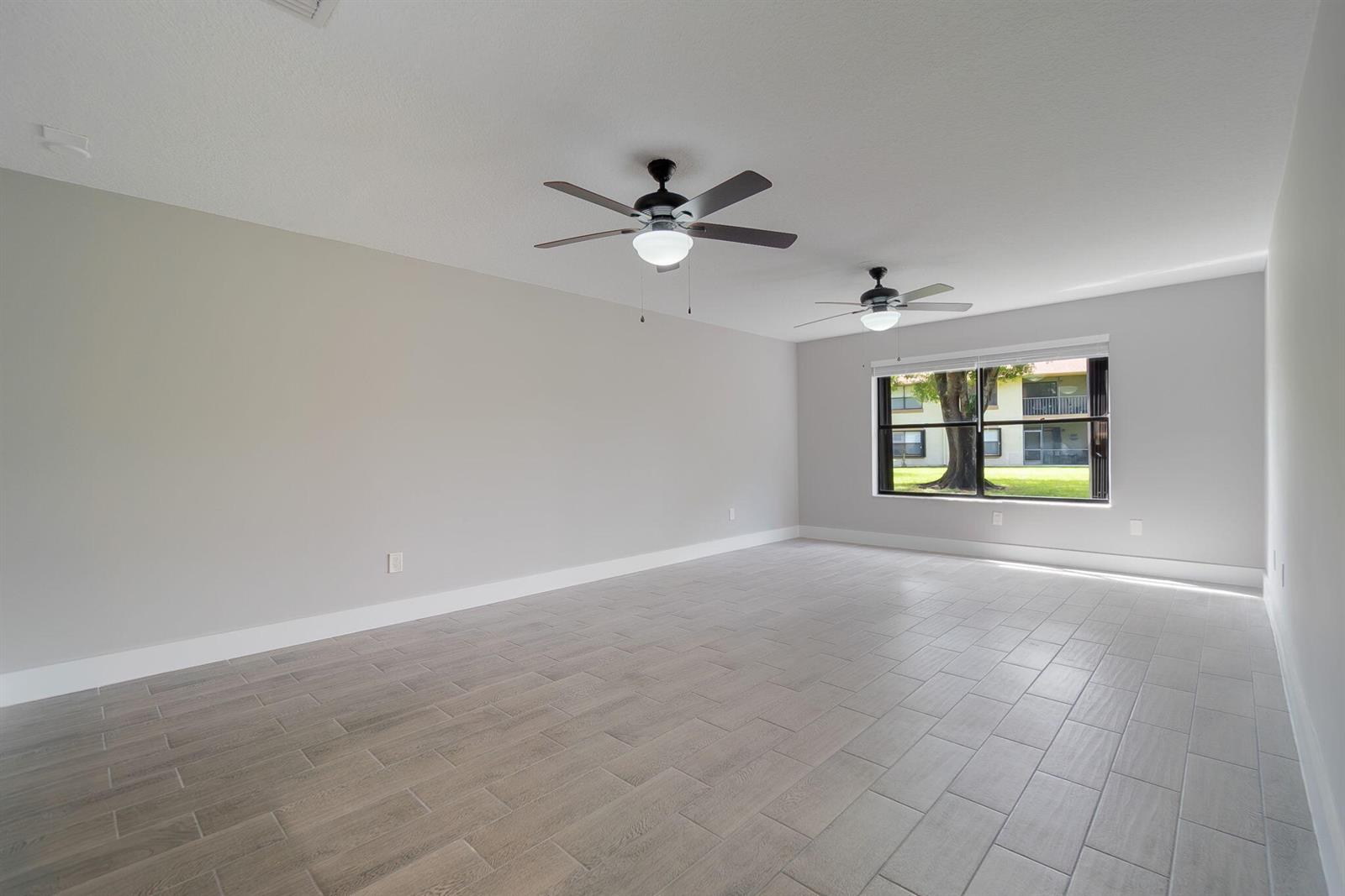 An empty room with light gray walls, wood-look tile flooring, and two ceiling fans — WELLINGTON, FL