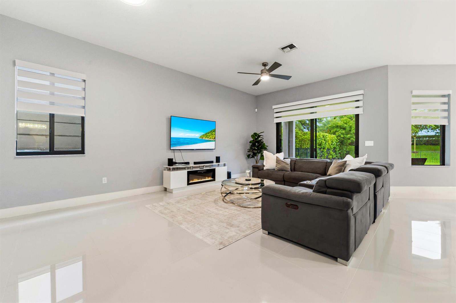 A living room features a grey sectional sofa, a wall-mounted television, and a fireplace console — 10555 Waves Way, Parkland FL 33076, PARKLAND, FL
