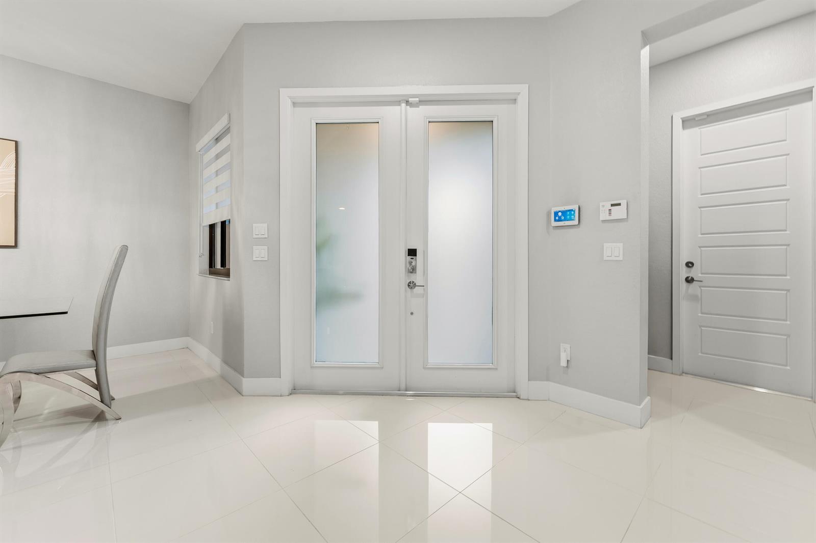 A bright entryway features white tile floors, double glass-paneled front doors, and a side door — 10555 Waves Way, Parkland FL 33076, PARKLAND, FL