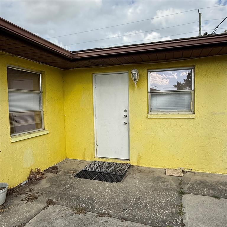 A yellow exterior wall features a white door, two windows, and a concrete patio area — 328 ORTIZ BOULEVARD UNIT B, NORTH PORT, FL
