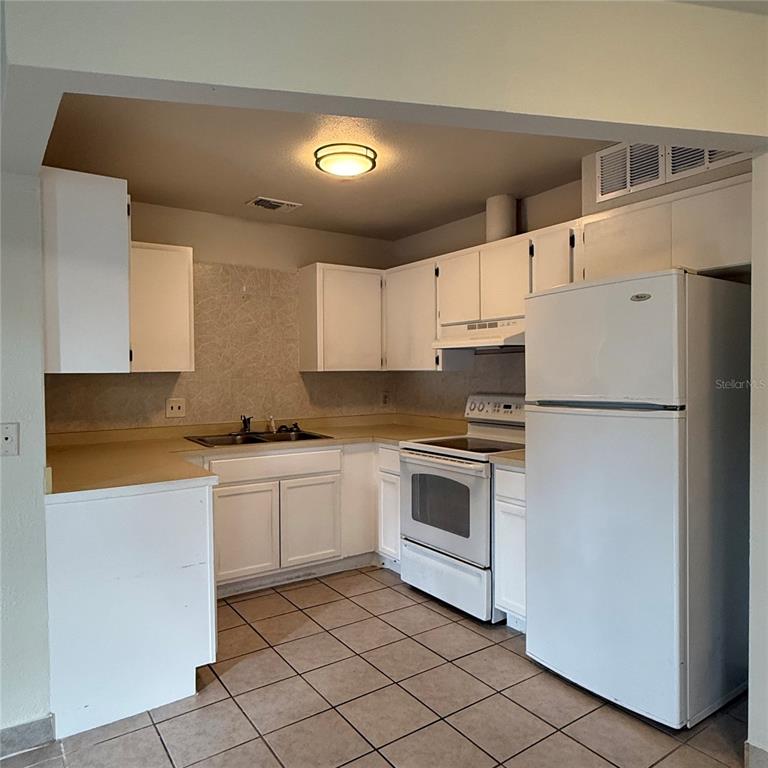 A kitchen features white cabinets, white appliances, tan countertops, and brown tile flooring — 328 ORTIZ BOULEVARD UNIT B, NORTH PORT, FL