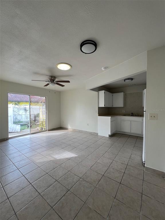 A tiled living room with a ceiling fan and sliding glass doors leads to a kitchen — 328 ORTIZ BOULEVARD UNIT B, NORTH PORT, FL