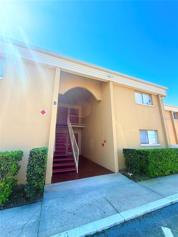 An exterior view of a two-story apartment building with a central staircase and tan stucco — 1000 LAKE OF THE WOODS BOULEVARD UNIT 101B, CASSELBERRY, FL