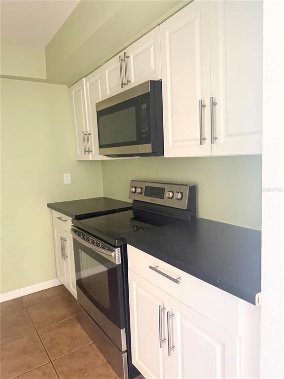 A kitchen features white cabinets, stainless steel appliances, and black countertops against light green walls — 1000 LAKE OF THE WOODS BOULEVARD UNIT 101B, CASSELBERRY, FL