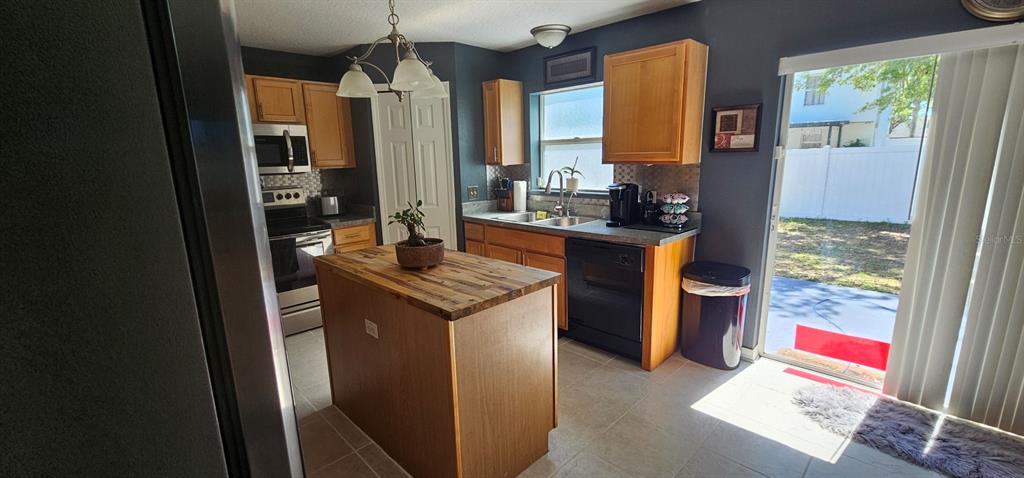 A kitchen features wood cabinets, a butcher block island, black appliances, and a sliding glass door — 921 WESTCLIFFE DRIVE, WINTER GARDEN, FL