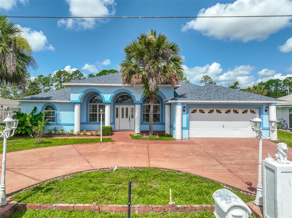 A light blue single-story house with a palm tree, arched windows, and a circular driveway — 4 RAINSTONE LANE, PALM COAST, FL