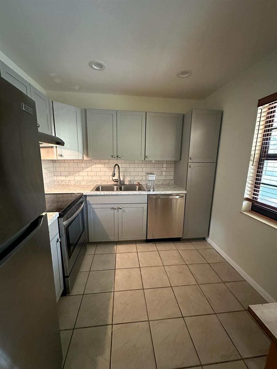 A kitchen features gray cabinets, stainless steel appliances, a subway tile backsplash, and tile flooring — 132 S Cypress Road # 523, Pompano Beach FL 33060, POMPANO BEACH, FL
