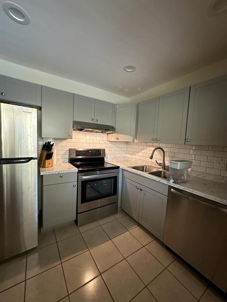 A kitchen features gray cabinets, stainless steel appliances, white subway tile backsplash, and tiled floors — 132 S Cypress Road # 523, Pompano Beach FL 33060, POMPANO BEACH, FL