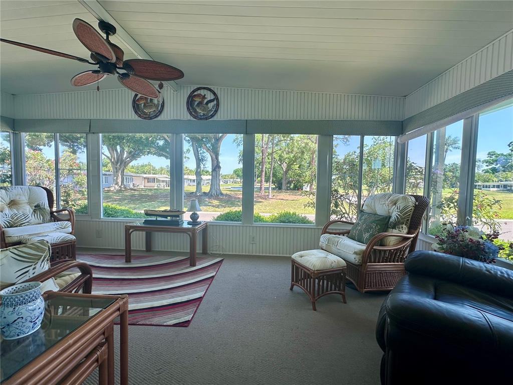 A sunroom features a ceiling fan, wicker furniture, a striped rug, and large windows — 1100 BELCHER ROAD S UNIT 304, LARGO, FL