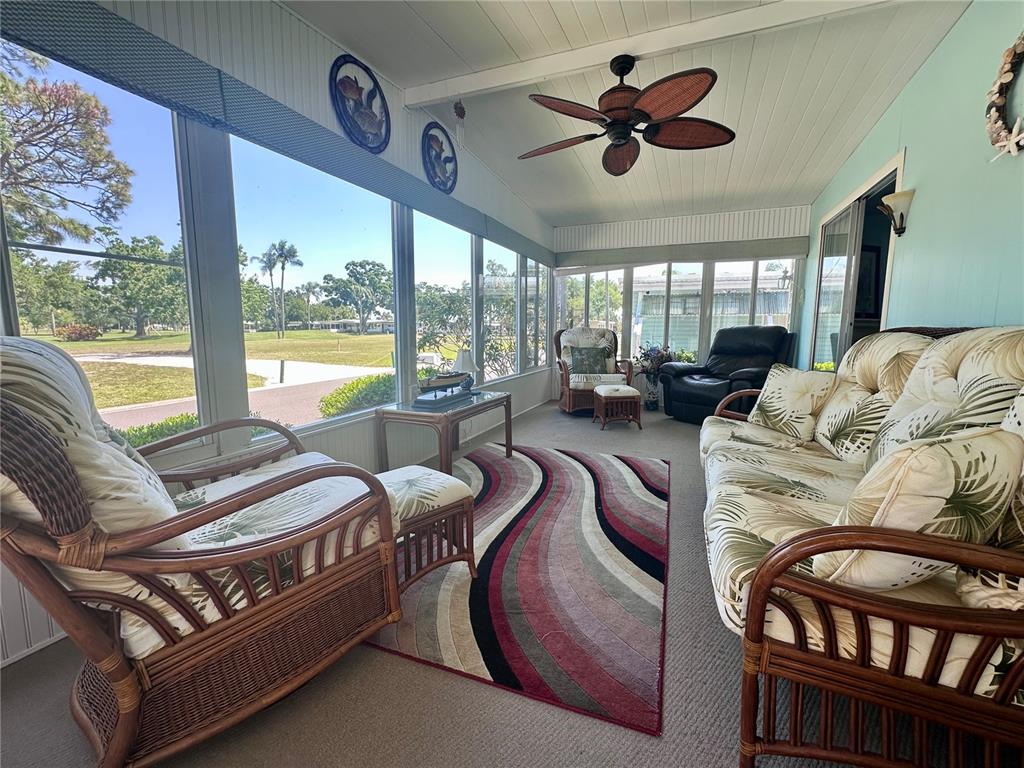 A sunroom features wicker furniture, a patterned area rug, a ceiling fan, and large windows — 1100 BELCHER ROAD S UNIT 304, LARGO, FL