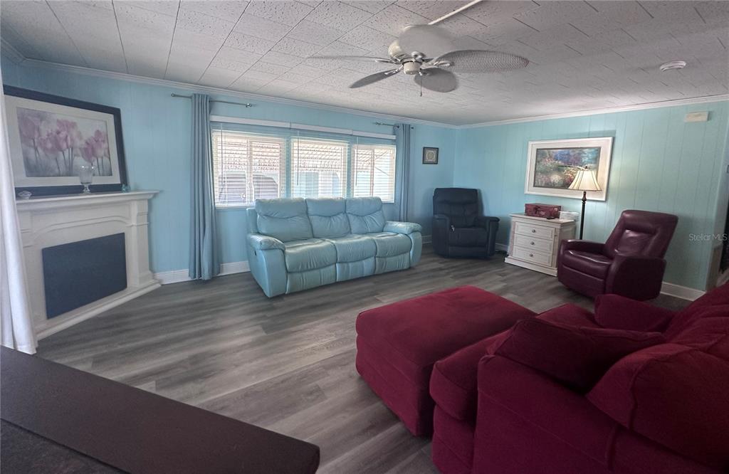 A living room features light blue walls, wood-look flooring, a fireplace, and multiple seating areas — 1100 BELCHER ROAD S UNIT 304, LARGO, FL