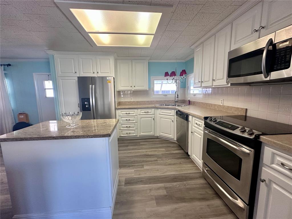 A kitchen features white cabinets, stainless steel appliances, a granite-topped island, and wood-look flooring — 1100 BELCHER ROAD S UNIT 304, LARGO, FL