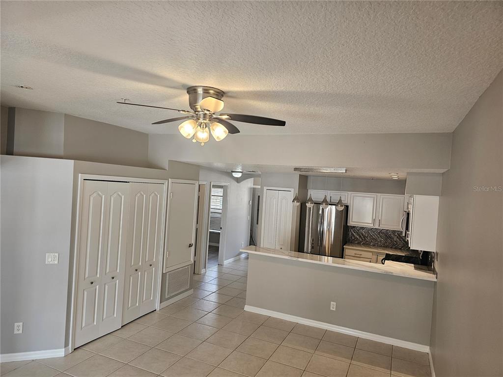A kitchen with white cabinets and a breakfast bar opens into a tiled living area — 673 SANDY NECK LANE UNIT 103, ALTAMONTE SPRINGS, FL