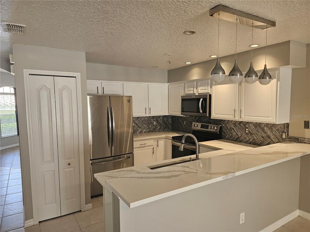 A kitchen features white cabinets, stainless steel appliances, a herringbone backsplash, and a quartz countertop — 673 SANDY NECK LANE UNIT 103, ALTAMONTE SPRINGS, FL