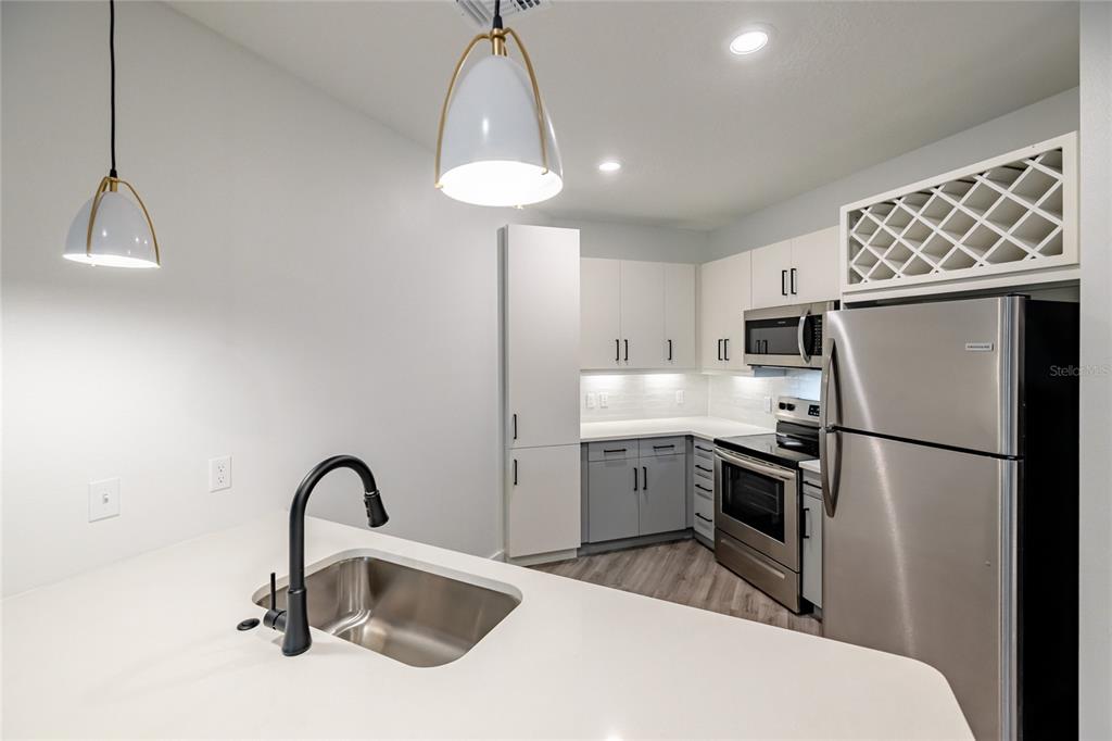 A modern kitchen features white cabinets, stainless steel appliances, a wine rack, and a sink island — 1420 LAKEFRONT DRIVE UNIT 7208, SARASOTA, FL
