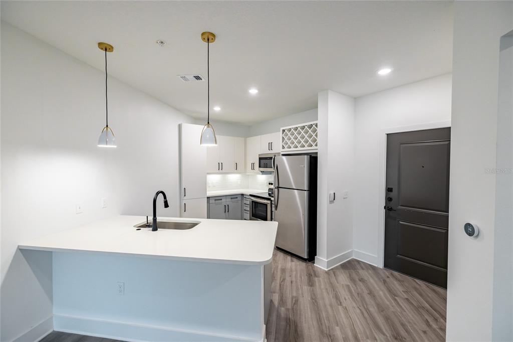 A modern kitchen features white cabinetry, stainless steel appliances, a kitchen island, and wood-look flooring — 1420 LAKEFRONT DRIVE UNIT 7208, SARASOTA, FL