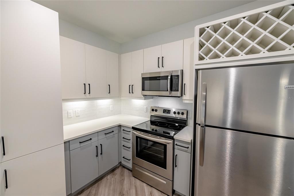 A kitchen features white upper cabinets, light gray lower cabinets, stainless steel appliances, and wine storage — 1420 LAKEFRONT DRIVE UNIT 7208, SARASOTA, FL