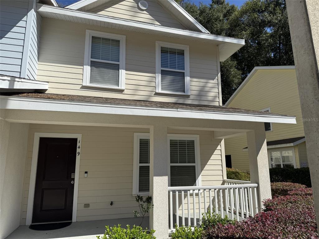 A two-story house exterior features light-colored siding, a covered front porch, and a dark door — 4639 SW 48TH DRIVE UNIT 149, GAINESVILLE, FL