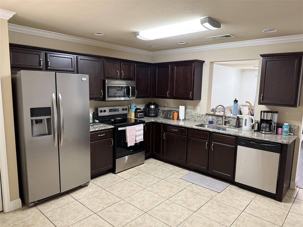 A kitchen features dark wood cabinets, granite countertops, stainless steel appliances, and tile flooring — 4639 SW 48TH DRIVE UNIT 149, GAINESVILLE, FL
